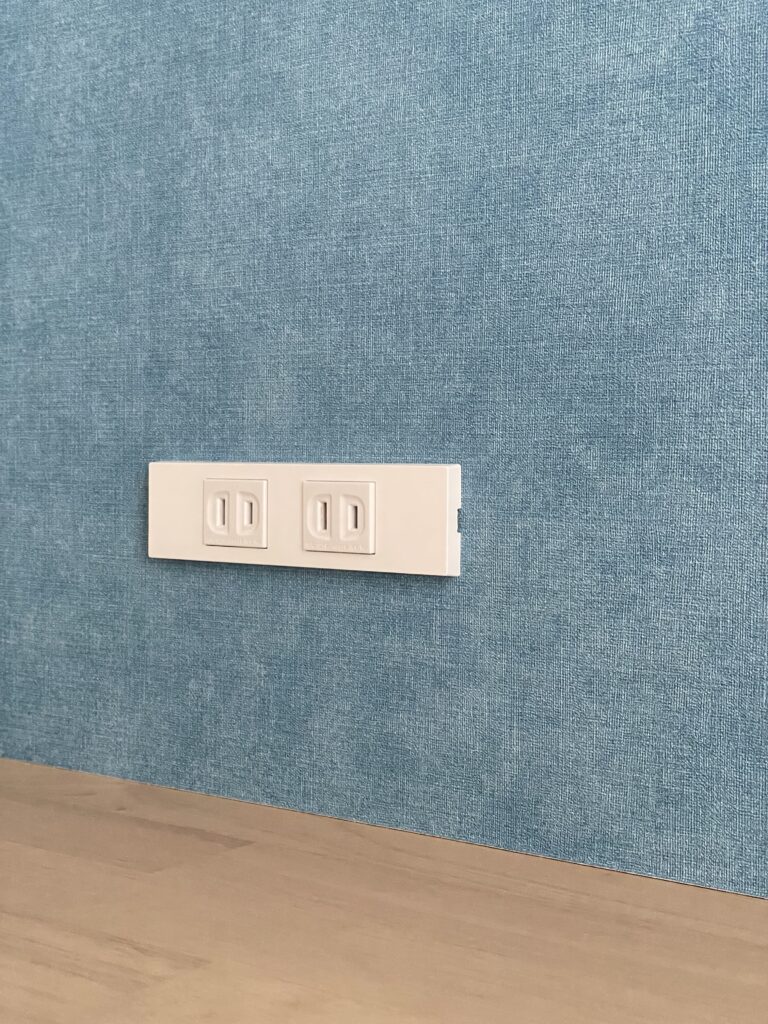 ２つのコンセントが横並びになっている部分をアップで撮影された写真。青色の壁紙の上に設置されている。