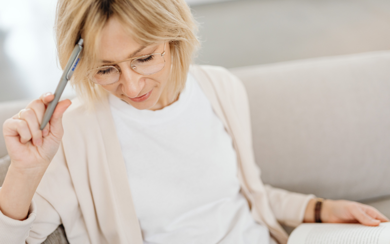 ペンを頭に当てて、考え事をするブロンドショートヘアの女性の写真。