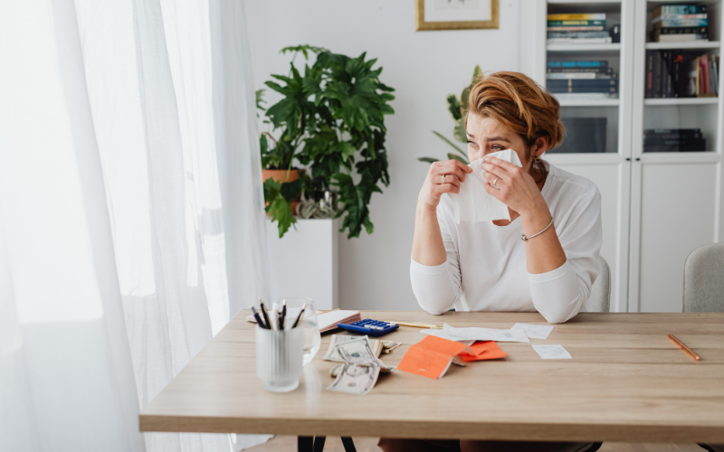 机に座る長袖白Tシャツの女性が、涙をティッシュで押さえながら座っている様子を撮影した写真。