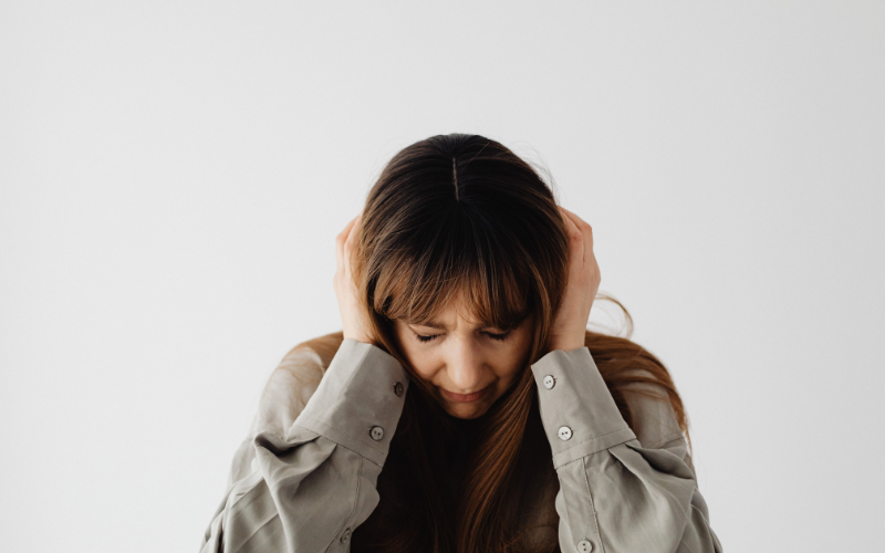 頭を抱えて悩む、茶髪女性の写真