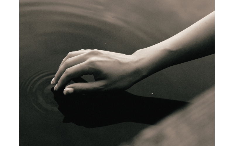 水たまりに手をかざしている様子を写したモノクロ写真