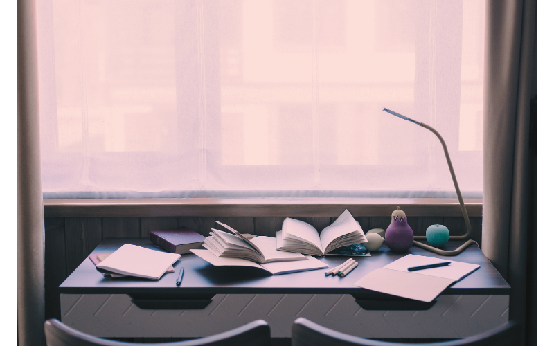 ノートや開いた本が並ぶ机の風景。個人の体験を整理し、構造として考え直すプロセスを表したイメージ。