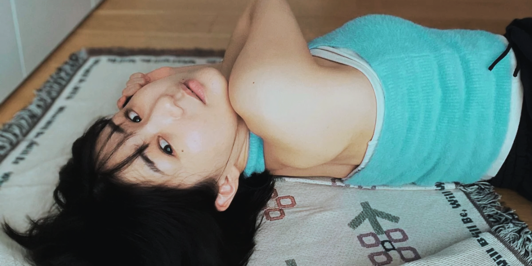 床に寝転びながら振り返る女性の後ろ姿。力が抜けた姿勢と柔らかな光が、安心と解放された状態を感じさせる