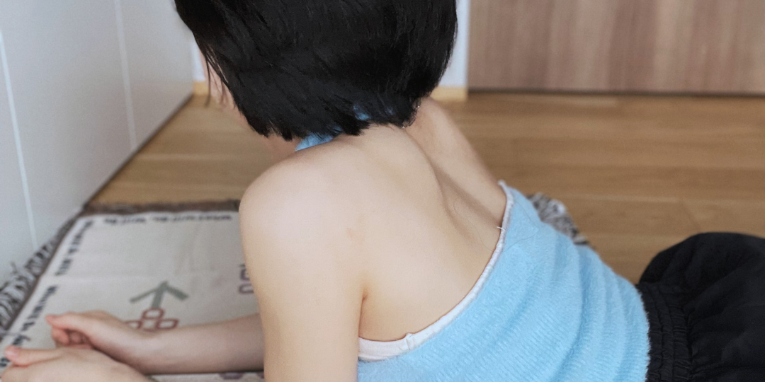 床に座り前を向く女性の後ろ姿。視線を外した静かな佇まいが、内側に意識が向いている状態を表している