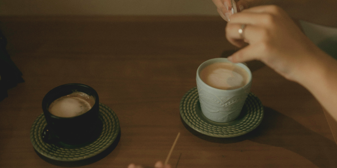 向かい合うテーブルで、コーヒーを前に会話している二人の手元。