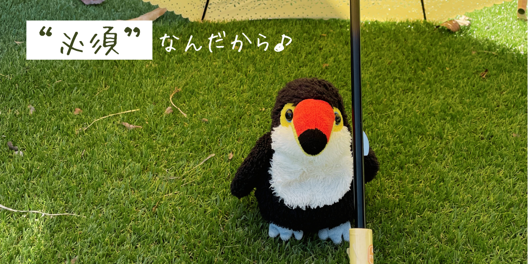 芝生の上で日傘の下に立つオニオオハシのぬいぐるみ「ねぐち」。紫外線を避けながら日差しを楽しむ様子